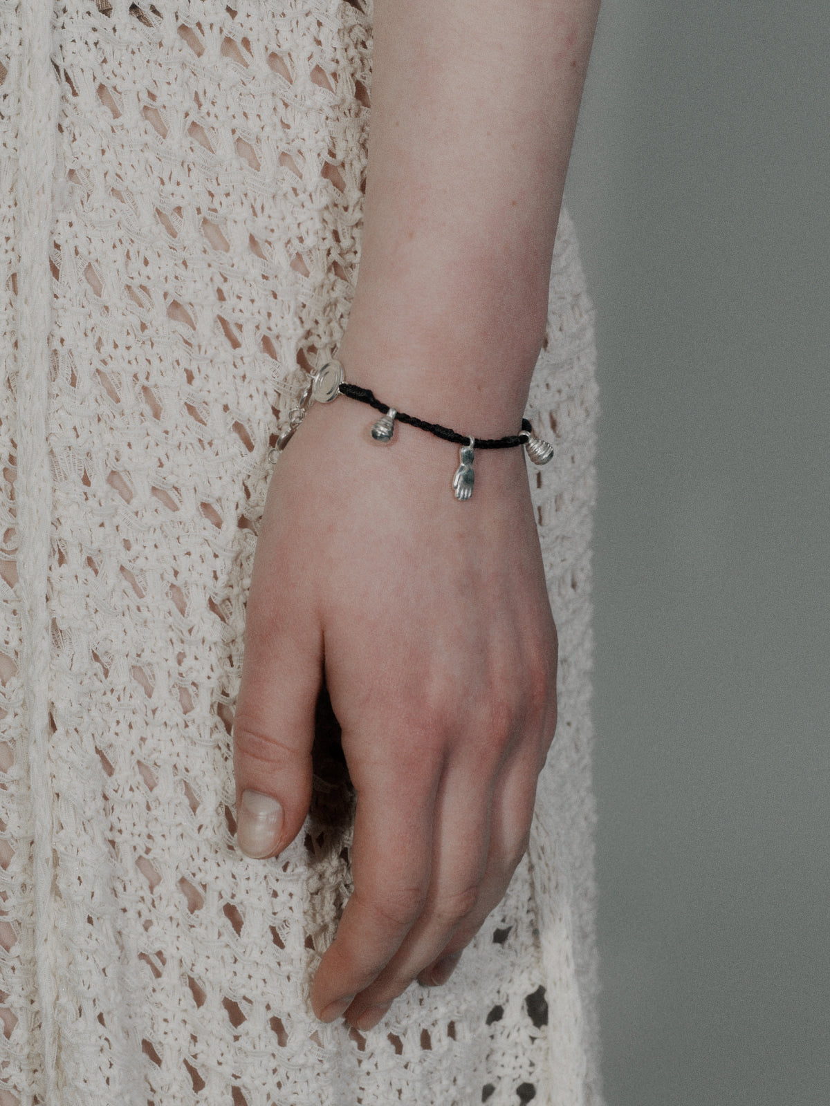 Hand-braided cord bracelet with black band and small silver charm dangles on wrist