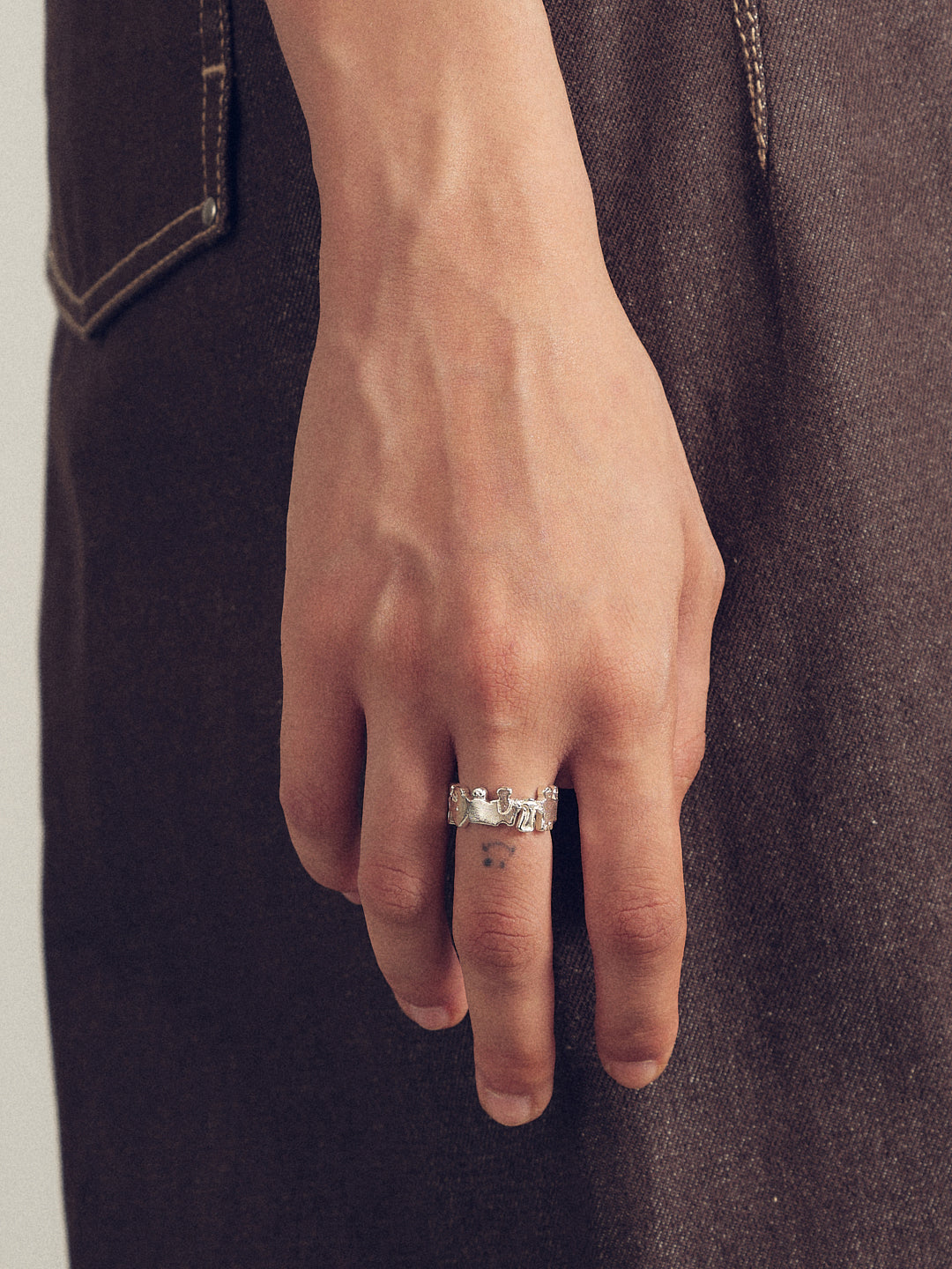 Silver ring on finger with small engraved crowd-like figures across the band