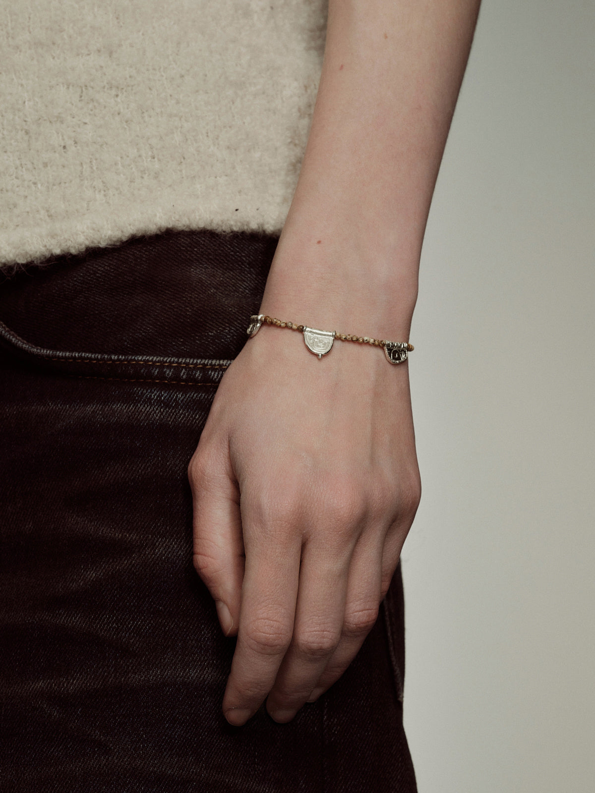 Silver beaded bracelet with small shield charm and clasp, worn on hand