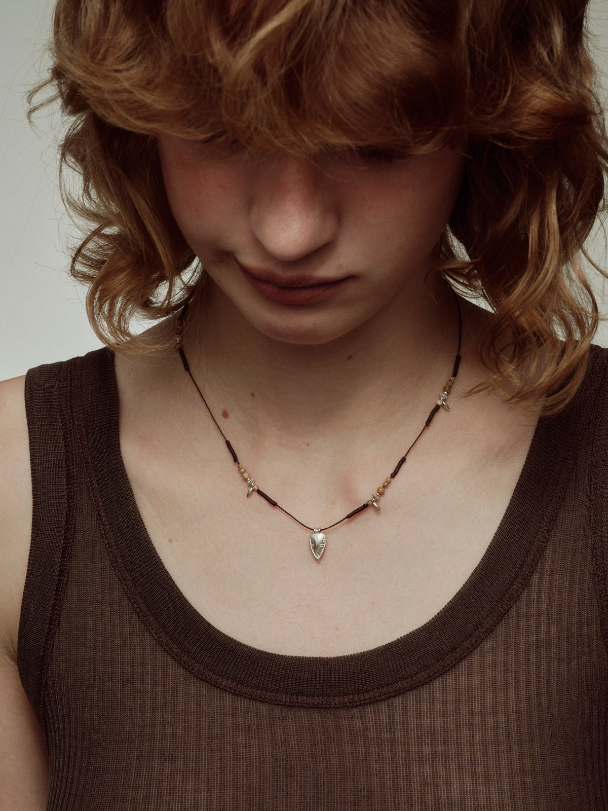Braided shield pendant necklace with black cord, gold beads, and silver shield centerpiece