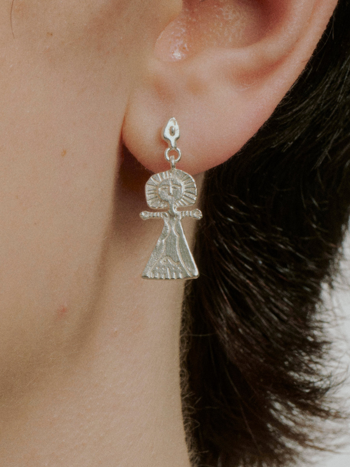Silver hoop earrings featuring a hanging angel figure charm with halo detail