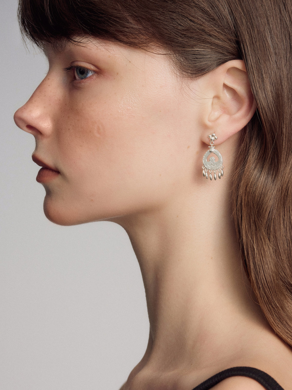 Silver dangling earrings with circular charm and hand dangles, close-up side