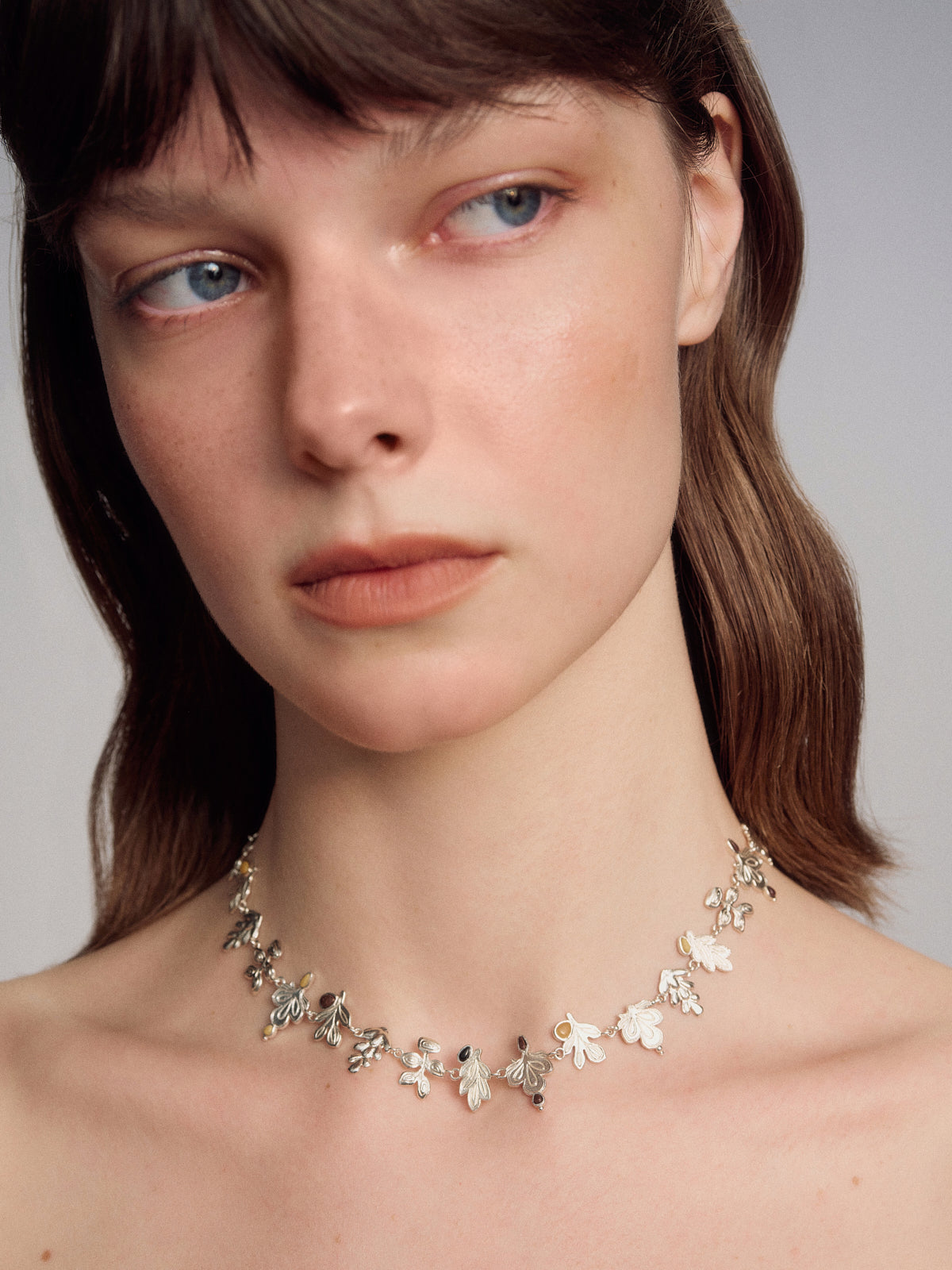Silver vine floral necklace with repeating blossom charms and curved chain
