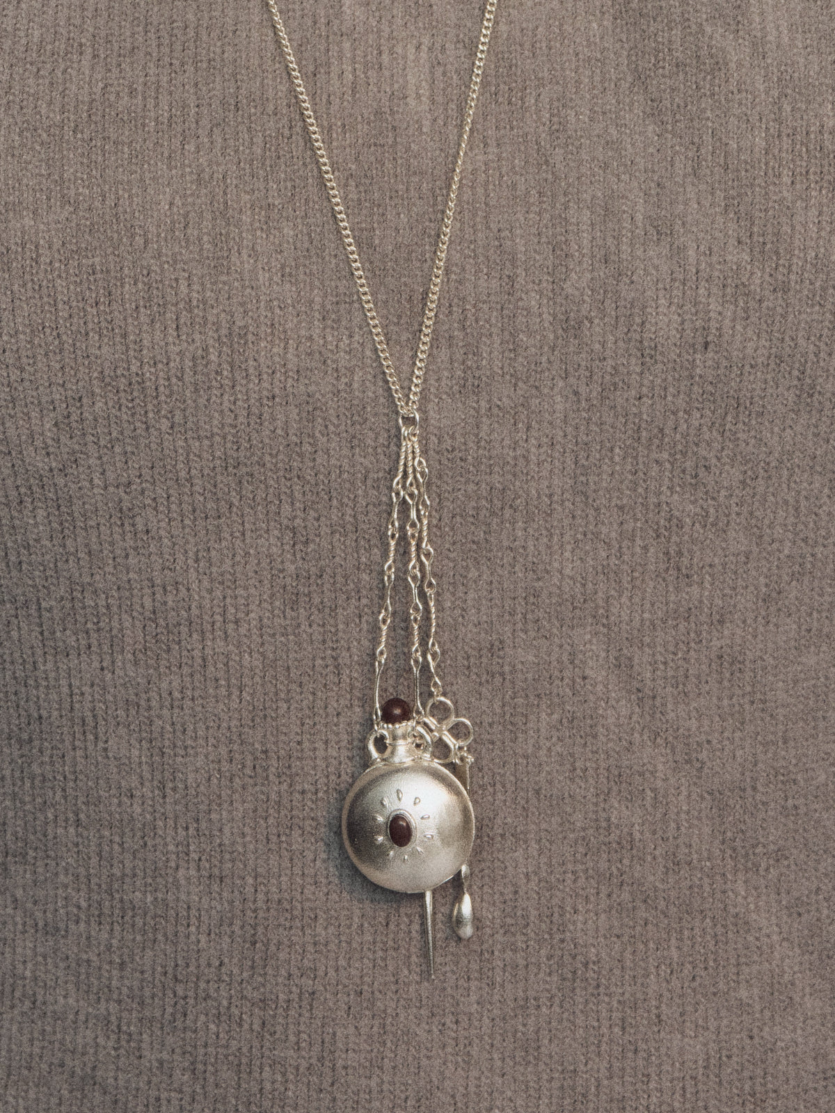 Silver long necklace with bottle-shaped charm pendant and red bead accent on top